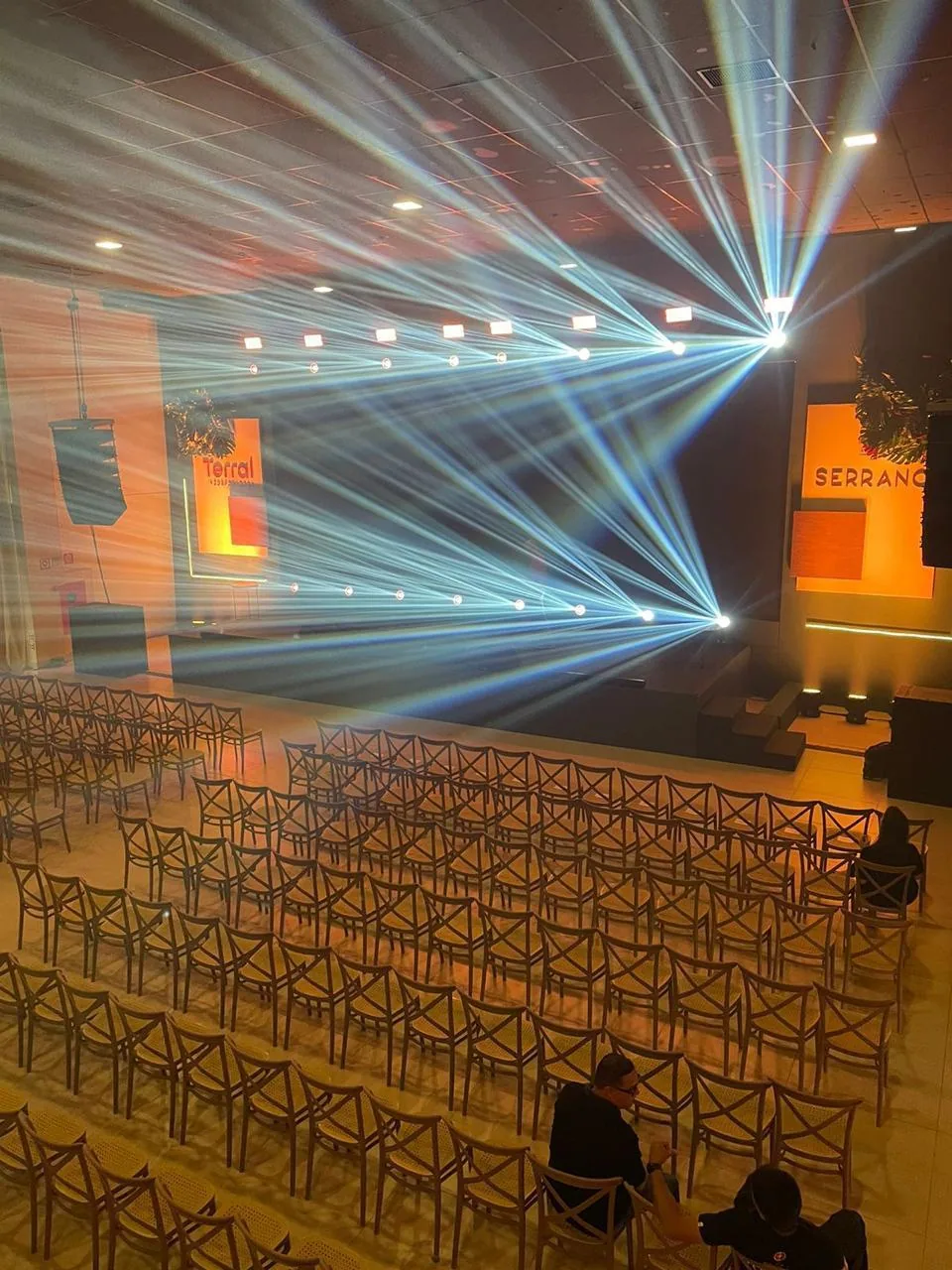 Salão em formato auditório com centenas de cadeiras e iluminação cênica no palco