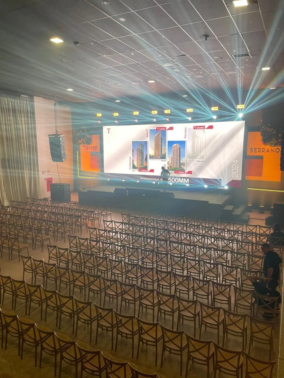 Salão montado em formato auditório para lançamento imobiliário, com telão e iluminação cênica