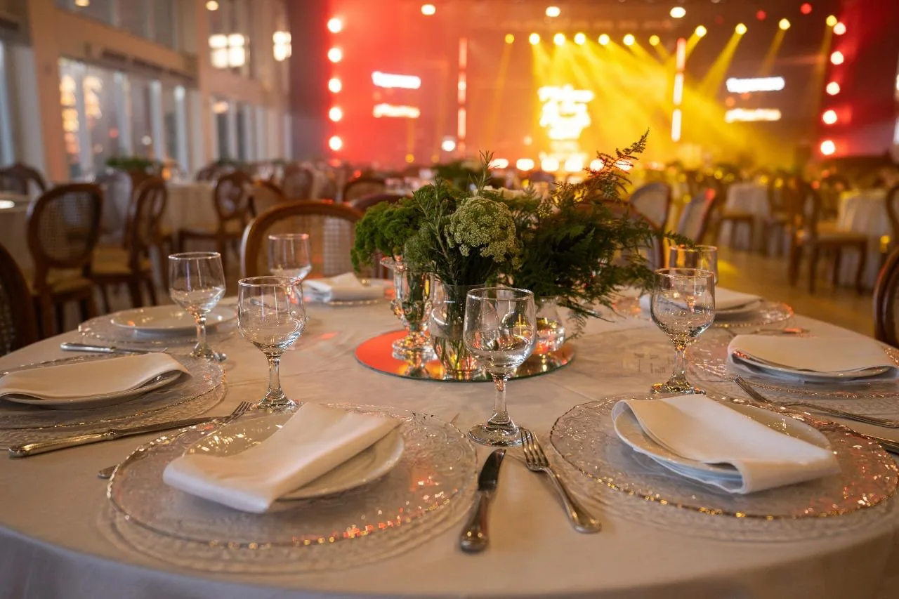 Mesa posta para jantar empresarial, com palco iluminado ao fundo